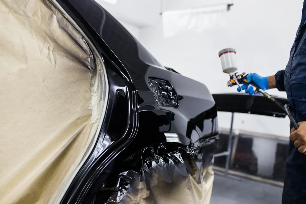 Autocarrozzeria Sciuto - A person using a spray gun to paint a black car, with protective covering around it. 