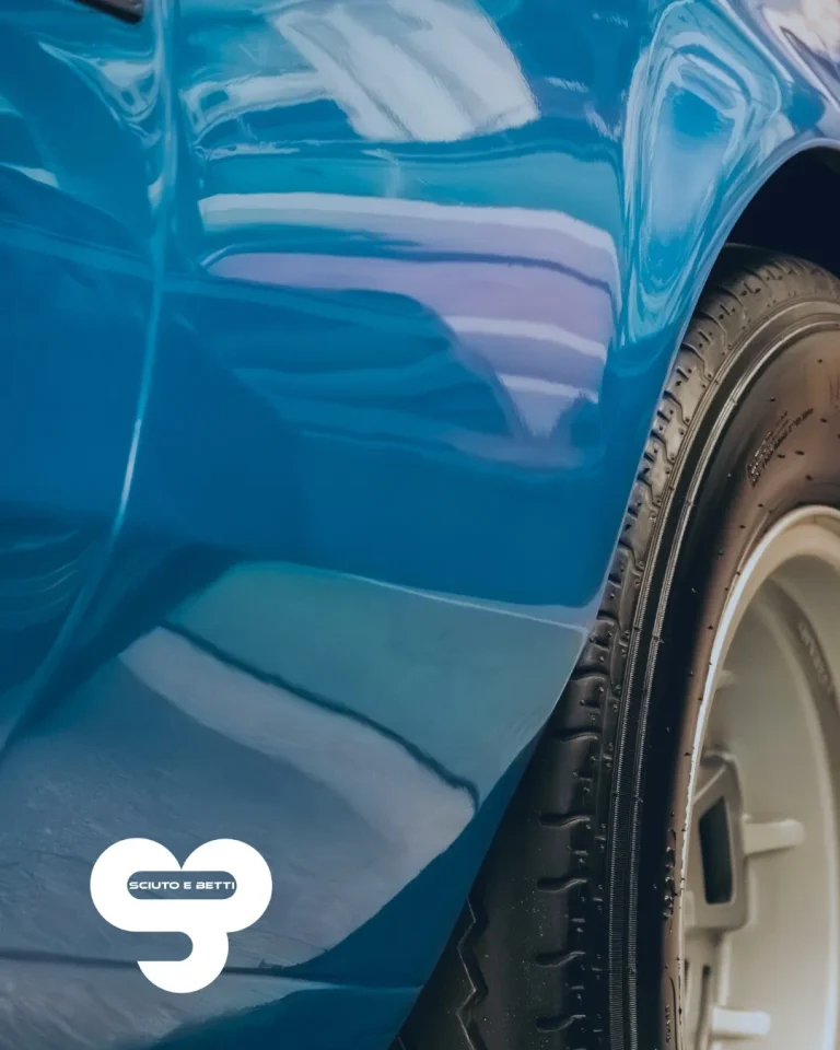 SCIUTO - Sistema tintometrico - Close-up of a shiny blue car's side and tire with reflections.